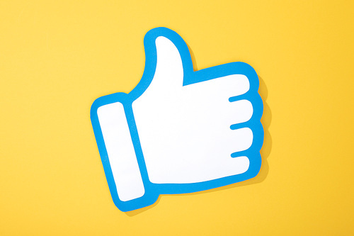 top view of white paper hand with thumb up on yellow background