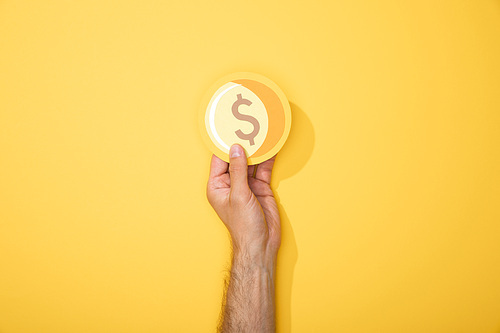 cropped view of man holding paper icon of golden coin on yellow background