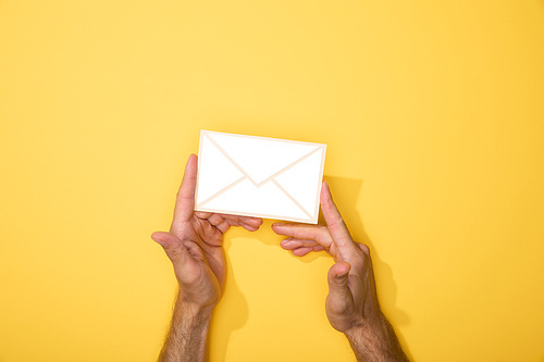 cropped view of man holding paper icon of envelope on yellow