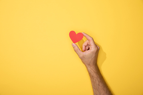 cropped view of man holding red paper heart on yellow