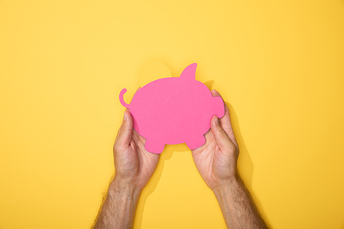 cropped view of man holding pink paper piggy bank on yellow