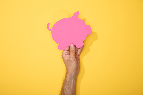 cropped view of man holding paper icon of pink piggy bank on yellow