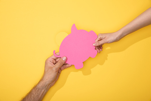 cropped view of man and woman holding paper piggy bank on yellow