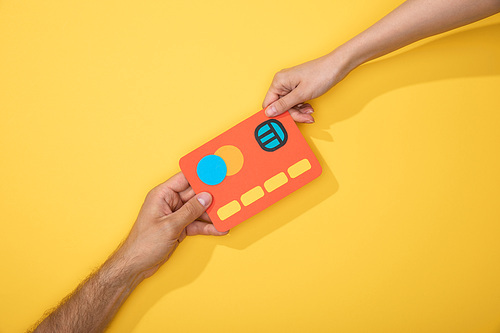 cropped view of man and woman holding paper icon of credit card on yellow