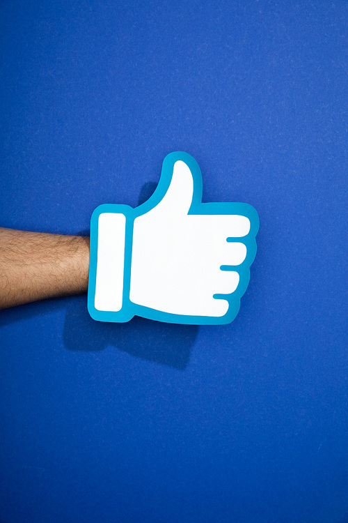 cropped view of man holding white paper thumb up on blue