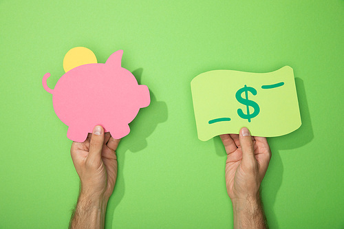 cropped view of man holding paper icons of piggy bank and dollar banknote on green