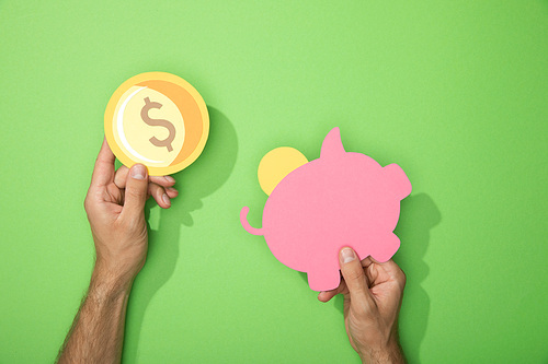 cropped view of man holding paper piggy bank and coin on green