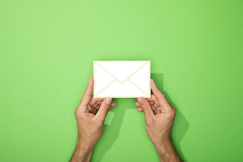 cropped view of man holding white paper icon of envelope on green