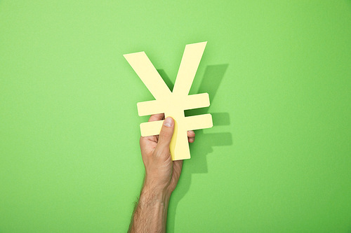 cropped view of man holding yellow yen currency sign on green