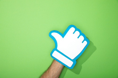 cropped view of man holding paper icon of thumb up on green