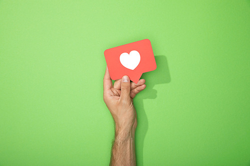 cropped view of man holding red paper icon with white heart on green