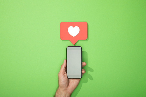 cropped view of man holding smartphone with heart in red icon above gadget on green
