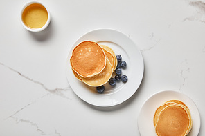 top view of bowl with honey near plates with pancakes