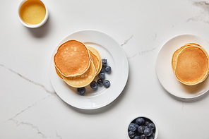 top view of plates with pancakes and two bowls with honey and blueberries