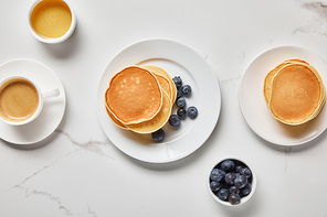 top view of bowls with blueberries and honey near plates with pancakes and cup of coffee