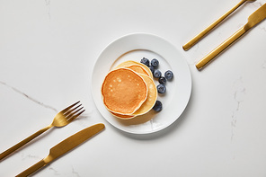 top view of plate with pancakes and blueberries near forks and knives