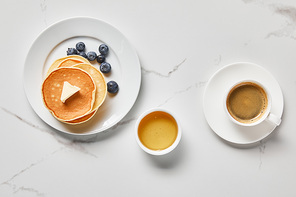 top view of bowl with honey, tasty pancakes with blueberries and cup of coffee