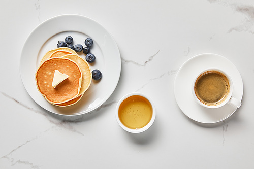 top view of bowl with honey, tasty pancakes with blueberries and cup of coffee