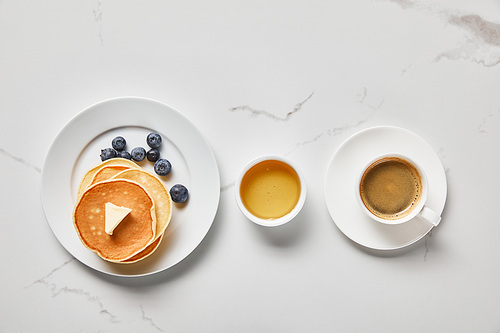 top view of bowl with honey, tasty pancakes with blueberries and butter, and cup of coffee