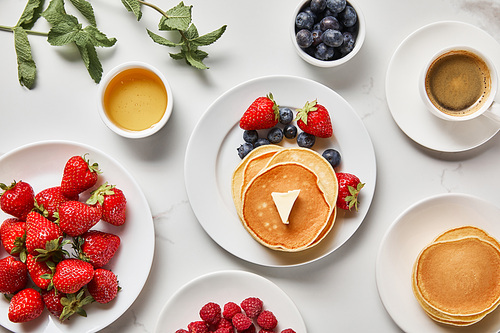 top view of healthy breakfast with strawberries, blueberries, raspberries, pancakes, honey and cup of coffee