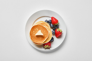 top view of white plate with pancakes, blueberries and strawberries