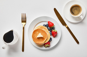 top view of pancakes, syrup in jug and cup of coffee near golden cutlery