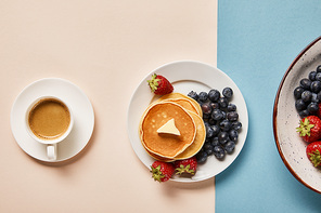 top view of pancakes with berries on plate near cup of coffee