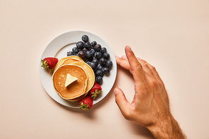 cropped view of man touching plate with pancakes and berries on pink