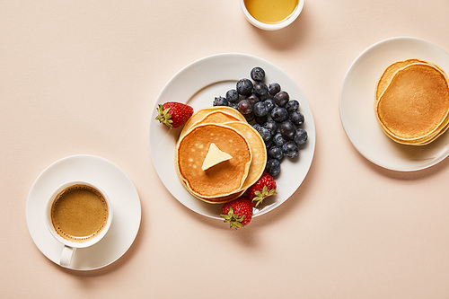 top view of pancakes with berries, near cup of coffee and bowl with honey on pink