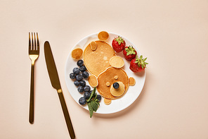top view of pancakes, blueberries and strawberries on plate near golden cutlery, bear concept
