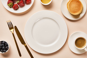 top view of served breakfast with berries, coffee, pancakes and empty plate in middle on pink background