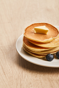 pancakes with butter and blueberries on plate on wooden surface