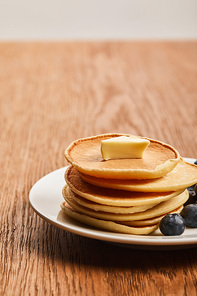 selective focus of pancakes with butter on plate on wooden surface