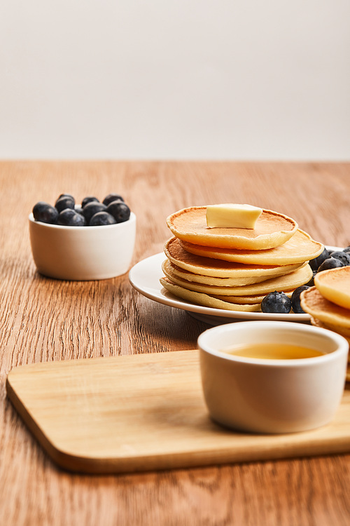 selective focus of pancakes with butter, blueberries and honey on wooden surface isolated on grey