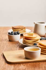 selective focus of plates with pancakes, berries, honey in bowl and syrup in jug isolated on grey
