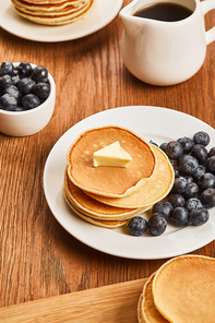breakfast with pancakes, butter, blueberries and syrup on wooden surface