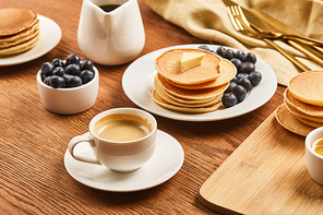 tasty breakfast with cup of coffee, pancakes and blueberries near linen cloth with cutlery on wooden surface