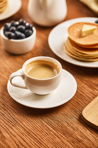 selective focus of cup of coffee with foam near plate with pancakes and bowl with strawberries