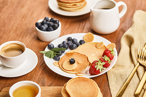 top view of pancakes with berries on plate, syrup in jug, honey and coffee, bear concept