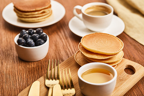 selective focus of pancakes near bowl with honey and blueberries, golden cutlery and cup of coffee