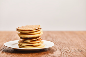 many tasty pancakes on white plate on wooden surface isolated on grey