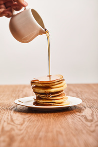 cropped view of man pouring pancakes on plate on wooden surface isolated on grey