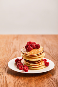 selective focus of pancakes with raspberries on plate on wooden surface isolated on grey
