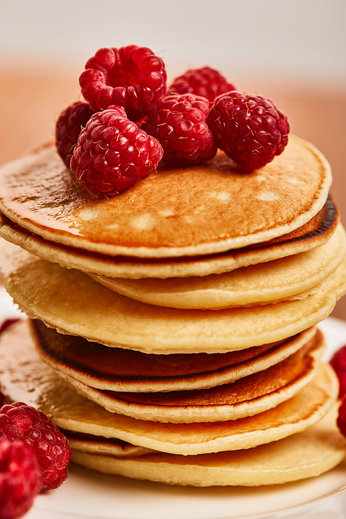 close up view of pancakes with raspberries on plate on wooden surface