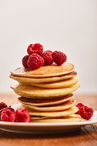 selective focus of tasty pancakes with raspberries on plate isolated on grey