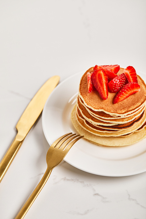 golden fork on plate with pancakes and strawberries and knife near plate