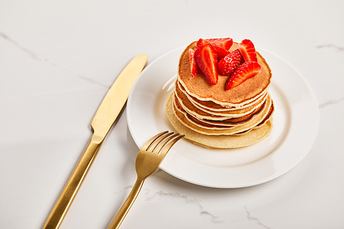 golden cutlery on plate with pancakes and strawberries