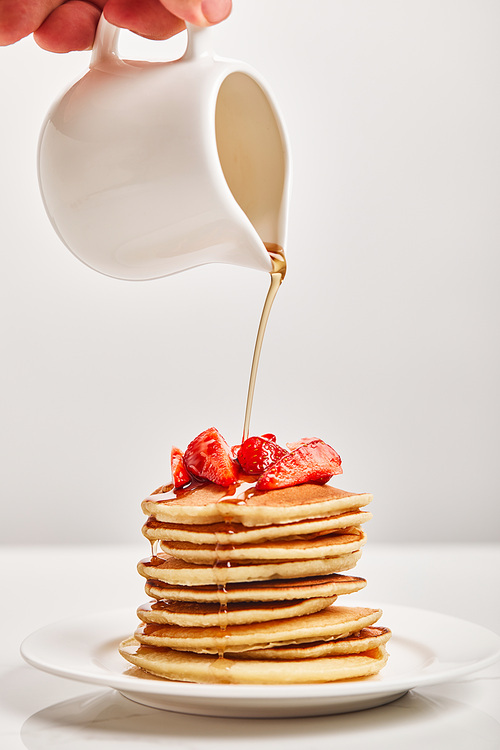 cropped view of man pouring pancakes with strawberries on plate isolated on grey