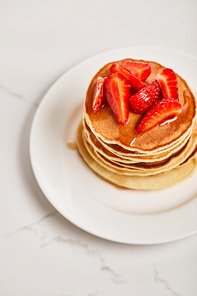 tasty pancakes with strawberries and syrup on white plate on textured surface