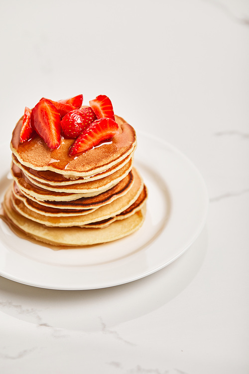 pancakes with strawberries and syrup on white plate on textured surface